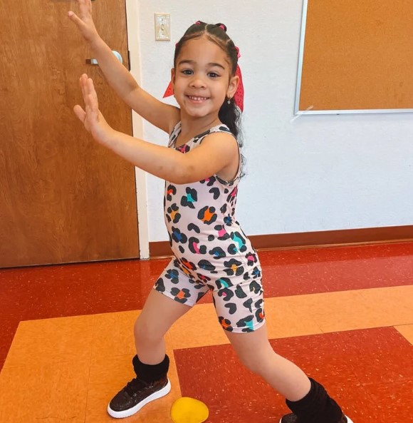 Young dancer in a colorful leotard and sneakers holds a strong pose in a dance studio